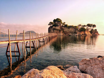 Pier leading towards island in sea at sunset