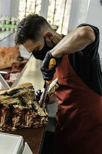 Butcher with mask preparing and cutting meat