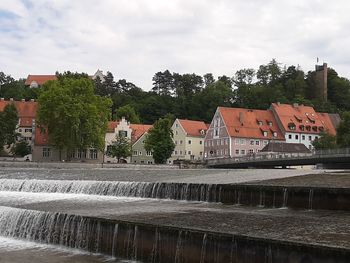 Houses by river against buildings in city against sky