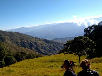 Female hikers on field at mountain against clear blue sky during sunny day