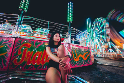 Portrait of young woman sitting on illuminated carousel at amusement park