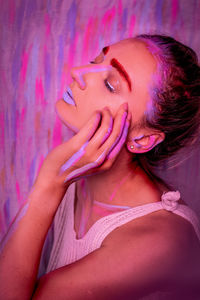 Young woman touching cheek against multi colored wall