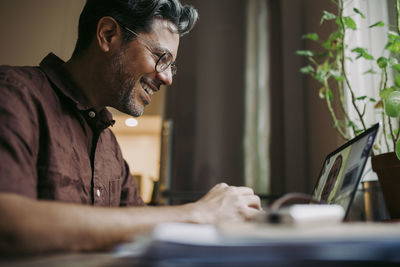 Happy businessman discussing with male entrepreneur while working on laptop at home