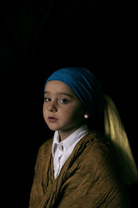 Portrait of young woman standing against black background