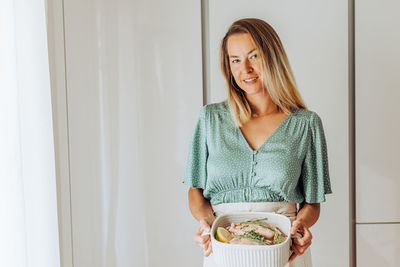 Young blond woman holding a tray with chicken and aromatic herbs