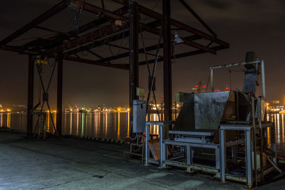 Empty chairs and tables by illuminated street against sky at night