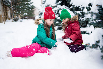 Wintertime. cute girls playing with snow, building an igloo. siblings having fun outside on snow day