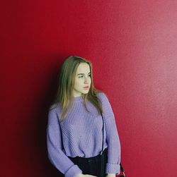 Portrait of young woman standing against red wall