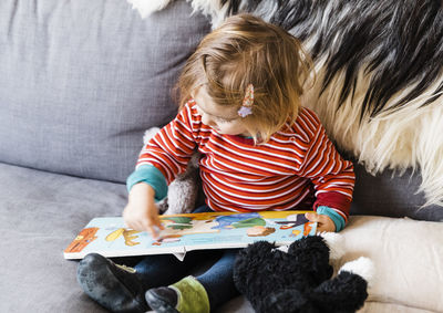 Cute girl playing with book while sitting on sofa at home