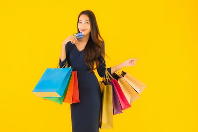 Smiling young woman standing against yellow background