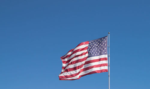 Low angle view of american flag waving against clear blue sky