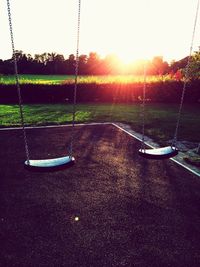 Empty swings at playground against sky during sunset