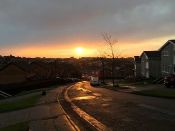 Road by houses against sky at sunset