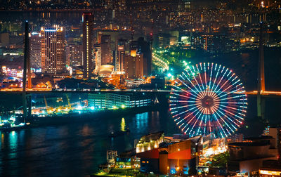 Illuminated ferris wheel by river in city at night