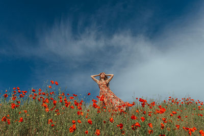 Beautiful girl in a dress in a poppy field against a blue sky with clouds