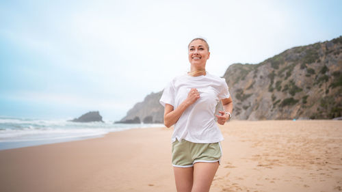 Portrait of young woman standing at beach against sky