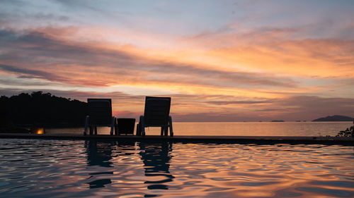 Silhouette swimming pool by sea against sky during sunset