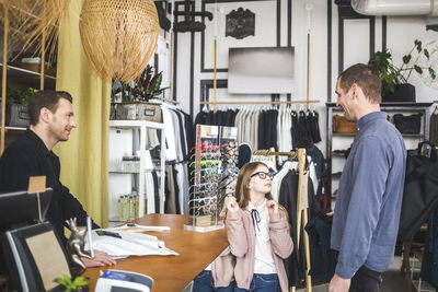 Cute daughter trying eyeglasses while looking at father by checkout counter in boutique