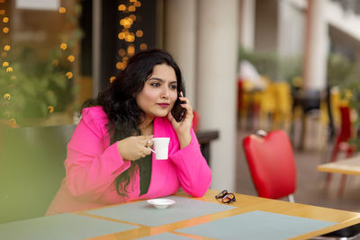 A smiling indian businesswoman is talking on her mobile phone and drinking coffee.