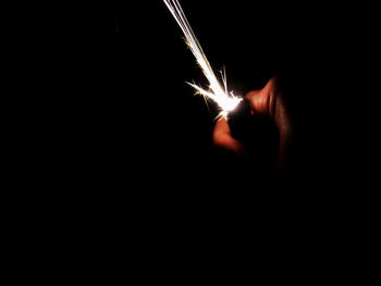 Midsection of person holding sparkler against black background