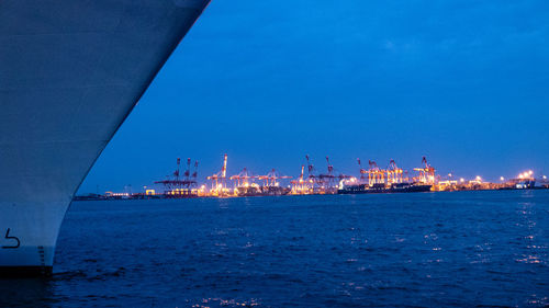 Illuminated harbor by sea against blue sky