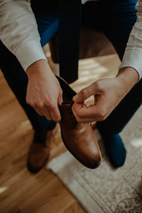 Low section of man holding shoe sitting on wooden floor