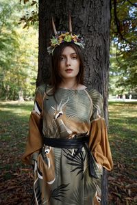 Portrait of woman standing by tree trunk