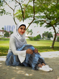 Young woman sitting on grass against trees