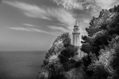 Lighthouse amidst sea and buildings against sky