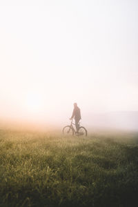 Silhouette man with bicycle on field against clear sky