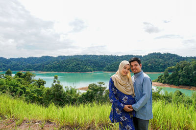 Young couple standing by lake against sky