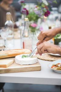 Cropped hands of man cutting mozzarella over cutting board at building terrace during party