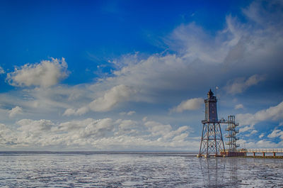 Lighthouse by sea against blue sky