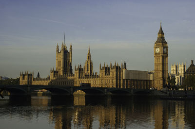 Bridge over thames river by buildings against sky