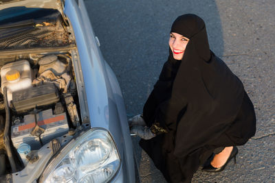 High angle portrait of woman wearing burka repairing vehicle on road