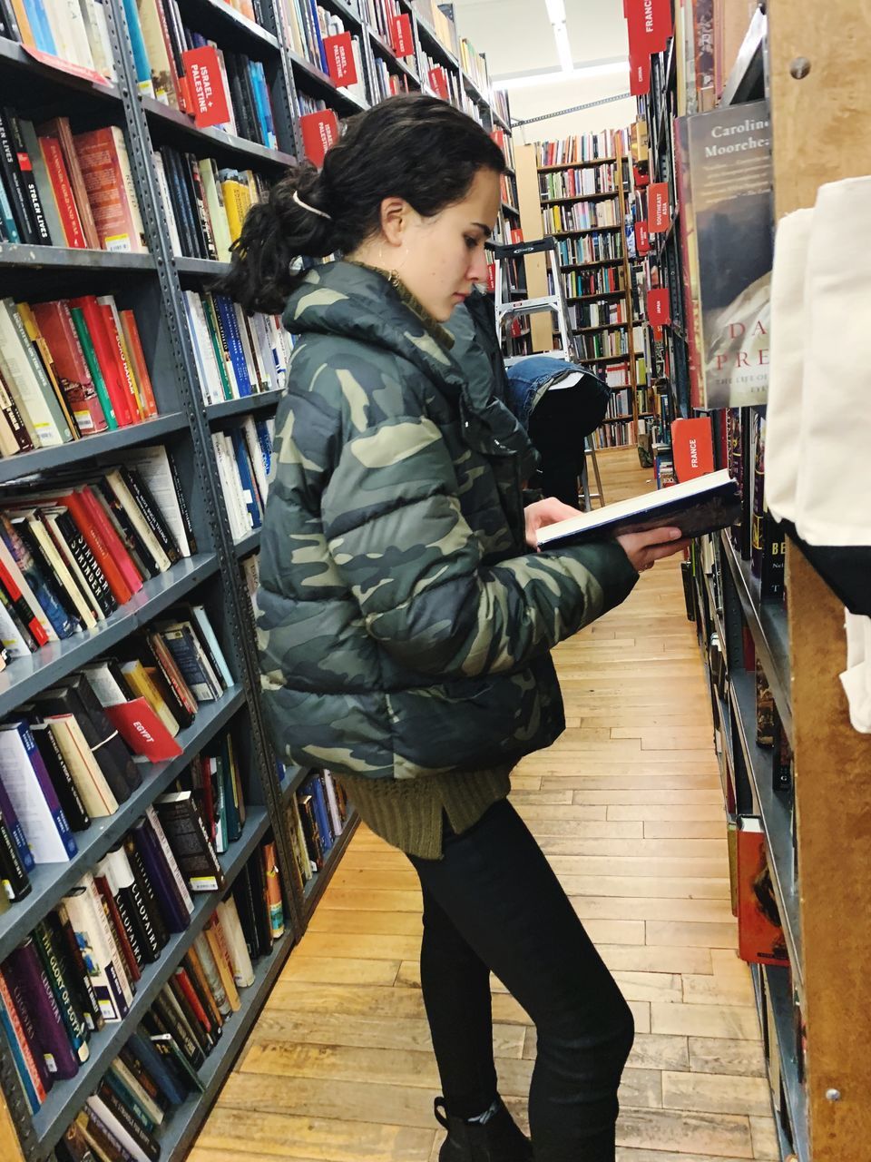 shelf, side view, standing, real people, indoors, one person, leisure activity, retail, publication, book, lifestyles, bookshelf, choice, store, shopping, holding, full length, casual clothing, young adult, consumerism, hairstyle