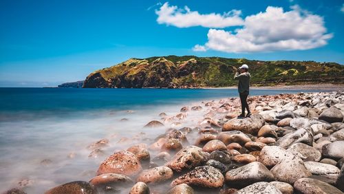 Man standing on rocks by sea against sky