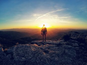 Full length rear view of hiker standing on cliff against sky at morning