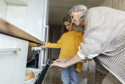 Grandmother and granddaughter taking freshly baked homemade bread out of the oven