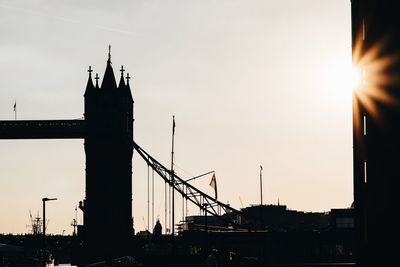 Silhouette cranes by bridge against sky during sunset