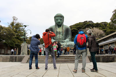 People walking by statue against sky in city