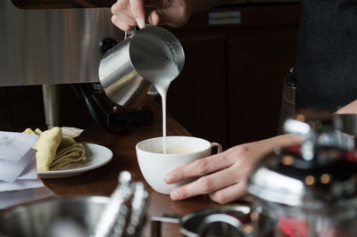 Close-up of person pouring milk in cup on table