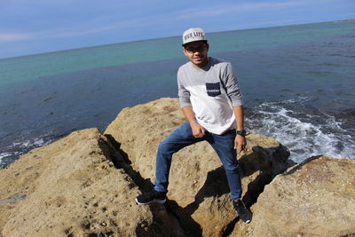 Portrait of young man standing on rock by sea