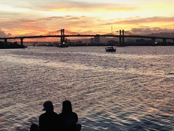 Silhouette people on bridge over sea against sky during sunset