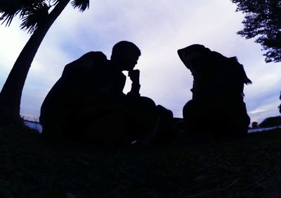 Silhouette man with dog sitting against sky