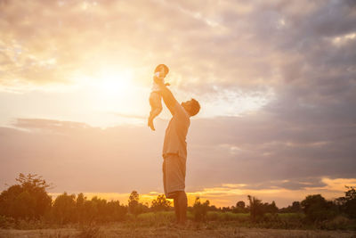 Side view of man standing on field against sky during sunset