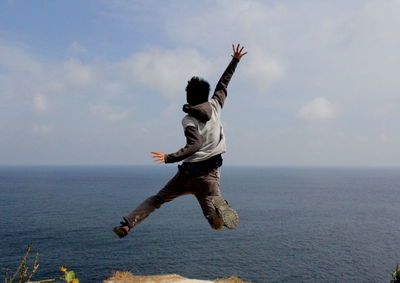 Rear view of man jumping against sea 