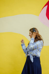 Portrait of young woman standing against yellow wall