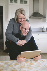 Smiling couple embracing and having video chat on tablet at kitchen table