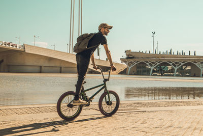 Man riding bicycle on bridge in city against sky